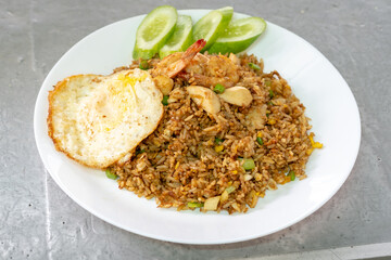 A plate of Indonesian nasi goreng, or fried rice, is served with shrimp, meatballs, a sunny-side-up fried egg, and slices of fresh cucumber.