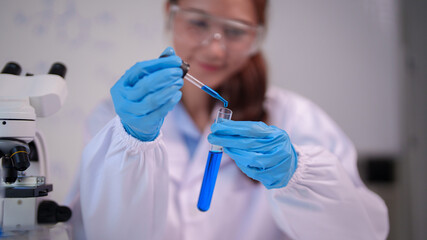 Asian adult scientist performs laboratory experiment using test tube dropper researching chemical solutions in modern science facility
