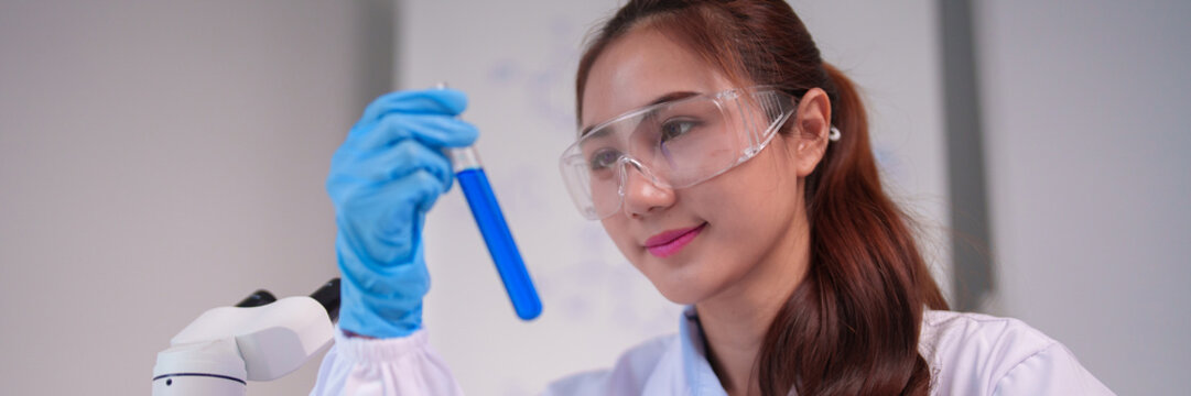 Asian adult woman scientist research working lab experiment chemistry analysis microscope blue liquid safety goggles scientific discovery development - Powered by Adobe