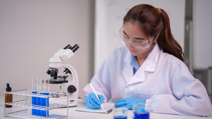 Asian woman scientist conducts laboratory research experiment writing notes study medical healthcare discovery innovation with microscope test tubes chemicals