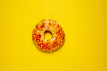 A single cheese bagel, seen from directly above, is centered on a plain, bright yellow background.