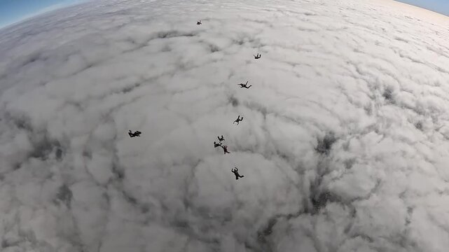 A group of skydivers speeding through the clouds in a spectacular sky.