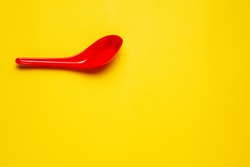 A top-down view of a single red plastic spoon resting in the top left corner of a bright yellow textured background.