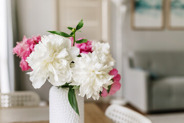 Bouquet of white and pink peonies in vase on table in cozy home interior.
