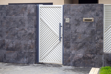 White diagonal slat gate in dark stone wall. Modern entrance with intercom and mailbox for luxury residential or commercial property. Real photo