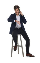Obraz premium Man in stylish jeans checking time while talking on smartphone against white background