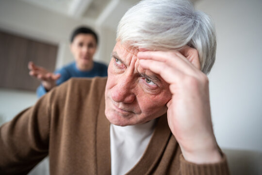 Close up exhausted senior husband silently bearing relentless verbal assault from shouting wife. Elderly man portrait, exhaustion of marital conflict, stressful criticism, mental fatigue suffering