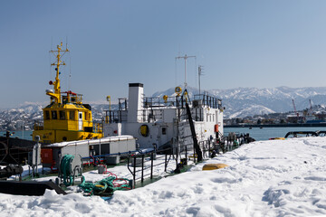 Yellow and white tugboats docked in snowy harbor with mountain view