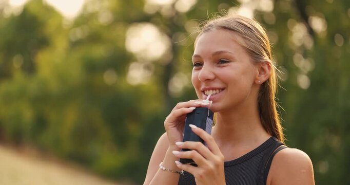 Young woman enjoys refreshing drink in outdoor park during golden hour
