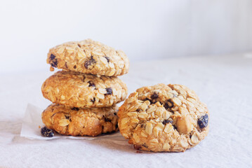 A freshly baked oatmeal raisin cookie with visible oats placed on natural linen tablecloth background.