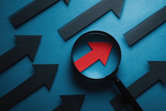 Concept illustration of a magnifying glass highlighting a red arrow amongst black arrows on a teal background