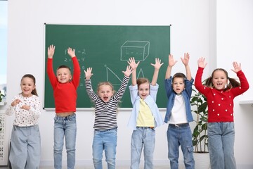 Group of happy pupils raising hands in front of chalkboard in elementary school
