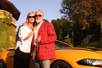 Naklejka premium Stylish senior couple in sunglasses near modern cabriolet outdoors