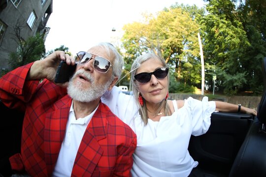 Senior woman and man talking on phone while enjoying cabriolet ride in city, wide angle lens