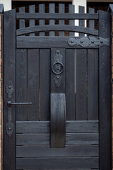 Black wooden gate with metal hardware, entrance to private property. Use in architecture, fencing systems, security design and urban landscape. Real photo