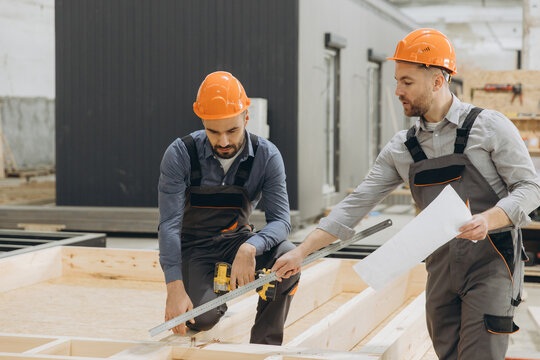 Construction workers measuring wooden planks for prefabricated building