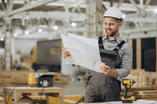 Smiling carpenter reading blueprints in a large lumber workshop