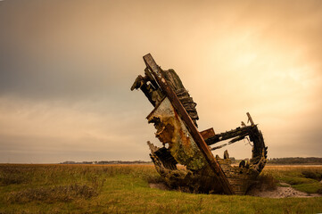 Decaying wooden shipwreck on salt marsh near Fylde under overcast sky