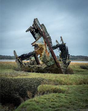 Decaying wooden shipwreck on salt marsh near Fylde under overcast sky