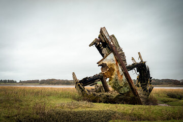 Decaying wooden shipwreck on salt marsh near Fylde under overcast sky