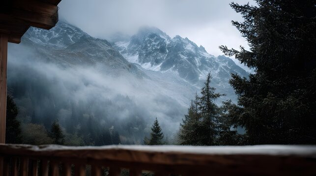 Atmospheric view of mist shrouded snow capped alpine mountains seen from a rustic wooden balcony