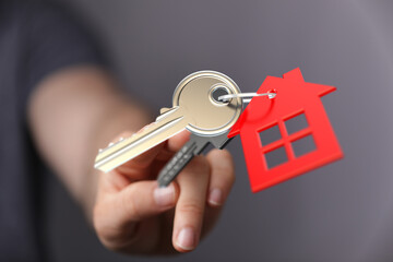 A person's hand holding keys with a red house charm. Represents homeownership, new home, real estate, buying or renting property. Focus on key,