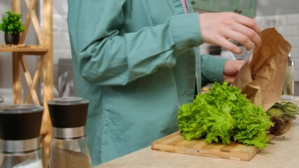 A woman is preparing a salad in a modern kitchen with fresh vegetables and kitchen utensils visible. - Powered by Adobe