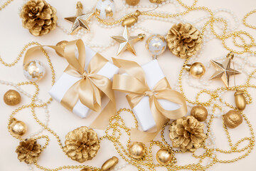 Two elegant gift boxes with golden ribbons surrounded by Christmas and New Year decorations. Flat lay with pine cones, stars, and pearls in soft golden tones