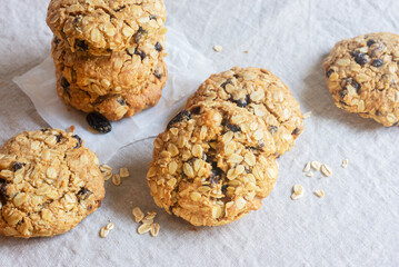 A freshly baked oatmeal raisin cookie with visible oats placed on natural linen tablecloth background.