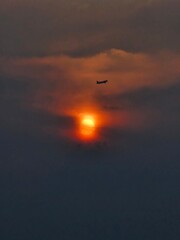 Airplane Flying Across Dramatic Sunset Sky with Glowing Sun and Cloud Layers