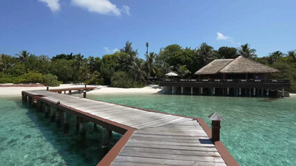 Luxury resort photo of Maldives tropical paradise island in Indian Ocean with palm trees, overwater thatched bungalows, wooden bridge. Beautiful photography, coral reef, azure ocean, sky with clouds. 