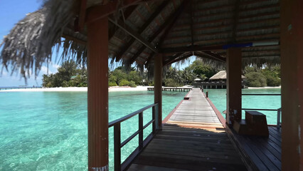 Luxury resort photo of Maldives tropical paradise island in Indian Ocean with palm trees, overwater thatched bungalows, wooden bridge. Beautiful photography, coral reef, azure ocean, sky with clouds. 