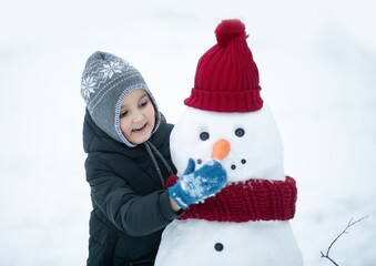 Cute little girl building snowman outdoor nature winter and playing with him. Children winter activity in Christmas time.