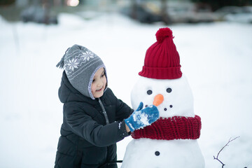 Cute little girl building snowman outdoor nature winter and playing with him. Children winter activity in Christmas time.