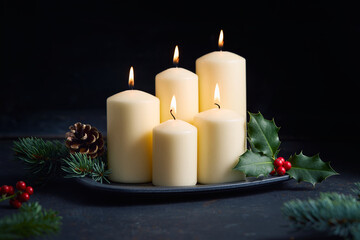 Burning candles with holly leaves, red berries, and pine branches creating a warm Christmas atmosphere.