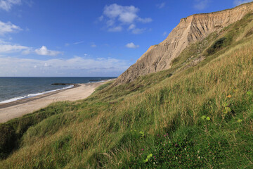 Landscape photo with a view of the North Sea coast, beach and rocky hills against a blue sky with clouds near Bovbjerg Lighthouse in Lemvig, Denmark