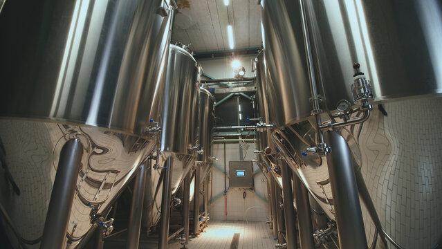 Shiny stainless steel fermentation tanks and conical vats standing in a modern brewery cellar, producing craft beverages for the industrial food and drink sector