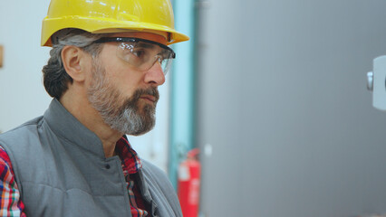 Engineer man, wearing yellow hard hat and safety glasses, focusing on his work in an industrial factory setting, representing expertise, safety, and dedication in the workplace