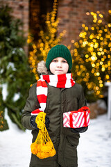 Happy cute teenager boy with mesh bag of tangerines standing near by spruce Christmas tree. Holiday celebrate concept.