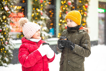 Happy little smiling girl and teen boy standing outdoor in a winter season and drinking cocoa. Holiday concept.