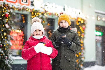 Happy little smiling girl and teen boy standing outdoor in a winter season and drinking cocoa. Holiday concept.