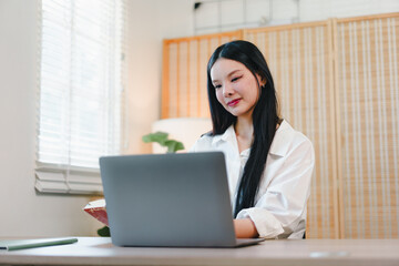Young woman working on laptop at home office desk with soft natural light and calm expression