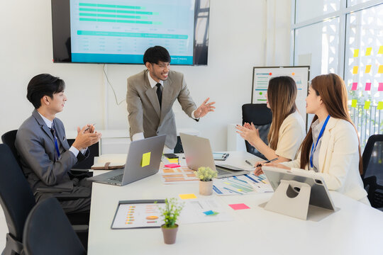 Teamwork concept of successful colleagues, multiethnic Asian team discussing business, clapping, laughing and smiling together in brainstorming meeting at office.