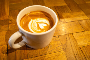 Hot latte, coffee with milk, and foam art on top in white ceramic cup on wooden table, in warm mood