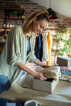 Young adult woman packing clothes in a box at home