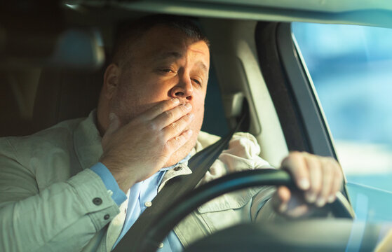 Mature man yawning while driving a car to work