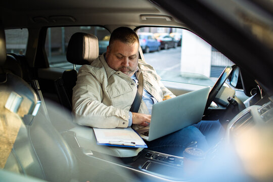 Middle aged man working on his laptop in a car while commuting to work