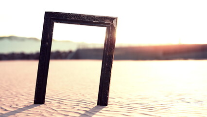 In a serene desert landscape, a striking black frame stands upright in the soft sand. The warm sunlight casts a golden hue, creating a captivating atmosphere that invites creativity and reflection.