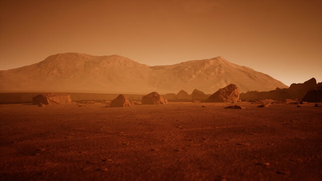 Barren terrain stretches across the surface of Mars, with rugged mountains rising in the background. Rocks dot the dusty ground as the orange light of twilight casts shadows across the landscape.