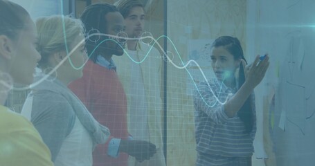 Brainstorming team writing on glass board in office with sticky notes, marker, line graph overlay